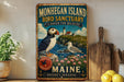 A vintage-style metal sign for the Monhegan Island Bird Sanctuary in Maine, featuring illustrations of puffins and seagulls on a rocky coastline with a lighthouse.