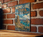 A vintage-style metal sign for the Mono Lake Tufa State Natural Reserve in California, featuring a scenic landscape with mountains, water, and a lake.