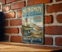 A vintage metal sign for the Monomoy National Wildlife Refuge, featuring a lighthouse and a bird, is displayed on a brick wall.