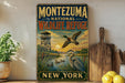 A vintage-style sign for the Montezuma National Wildlife Refuge in New York, featuring an illustration of ducks and a bird in flight against a sunset backdrop.