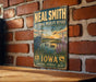 A vintage-style sign for the National Wildlife Refuge in Iowa, featuring an illustration of a heron and ducks in a lake, with the text "Neal Smith National Wildlife Refuge Iowa" and "Conserve - Protect - Enjoy".