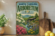 A vintage-style sign for the North Carolina Arboretum, featuring a scenic landscape with a waterfall, flowers, and a wooden bridge.