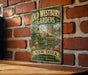 A vintage-style metal sign for Old Westbury Gardens, featuring a brick wall and a garden scene, is displayed on a wooden surface.
