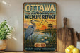 A vintage-style metal sign for the Ottawa National Wildlife Refuge in Ohio, featuring an illustration of a heron and a sunset over a lake.