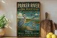 A vintage-style metal sign for the Parker River National Wildlife Refuge in Massachusetts, featuring an illustration of a heron and ducks in a grassy area with a river.