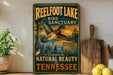 A vintage-style metal sign for Reelfoot Lake Bird Sanctuary, featuring an illustration of a bird in flight over a scenic landscape with a sunset.