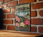 A vintage-style metal sign for the Rhododendron Species Botanical Garden in Washington, featuring a scenic landscape with a mountain and colorful flowers.