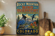 A vintage-style sign for the Rocky Mountain Bird Observatory in Colorado, featuring a blue bird perched on a mountain landscape with mountains, trees, and flowers.