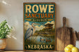 A vintage-style sign for Rowe Sanctuary Audubon in Nebraska, featuring an illustration of a bird in a pond and a wooden structure.