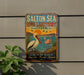 A vintage-style metal sign for the Salton Sea Bird Sanctuary in California, featuring illustrations of a pelican and flamingos against a sunset landscape.