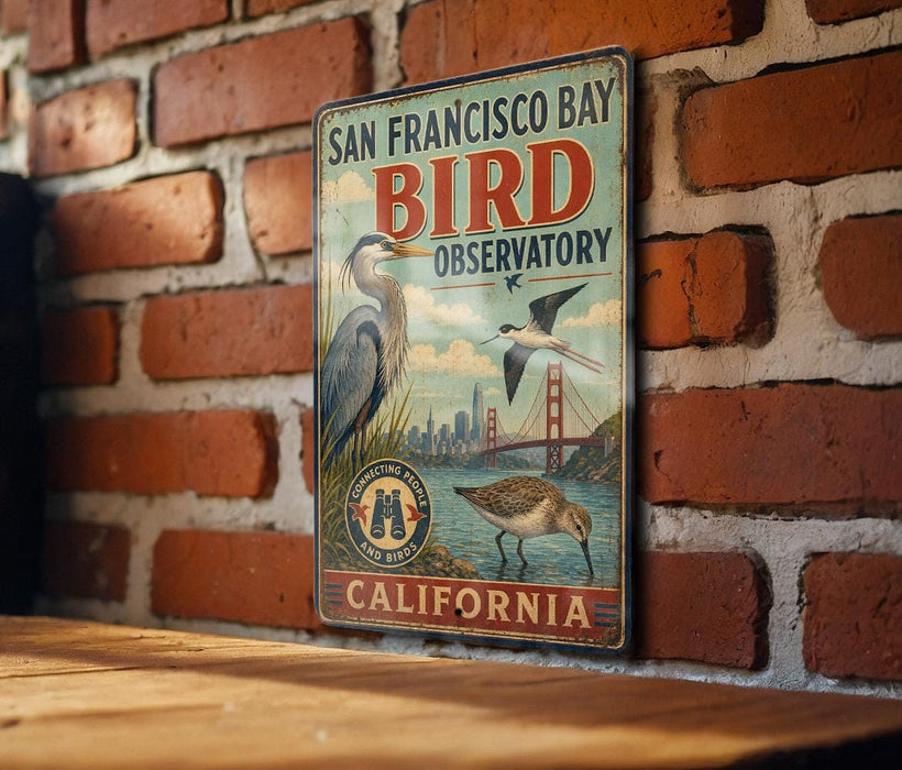 A vintage-style metal sign for the San Francisco Bay Bird Observatory in California, featuring illustrations of birds and a bridge.