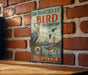 A vintage-style metal sign for the San Francisco Bay Bird Observatory in California, featuring illustrations of birds and a bridge.