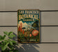 A metal sign with a colorful illustration of a garden and the text "SAN FRANCISCO BOTANICAL GARDEN" is displayed on a wall, with a plant to the left.