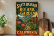 A vintage-style metal sign for Santa Barbara Botanic Garden in California, featuring a scenic landscape with mountains, palm trees, and colorful flowers.
