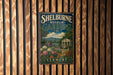 A vintage metal sign for Shelburne Museum Gardens in Vermont, featuring a scenic landscape with a house, garden, and mountains in the background.