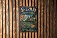 A vintage-style sign for Sherman Library & Gardens in Corona, California, featuring a tropical garden scene with palm trees and colorful flowers.