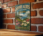 A vintage-style metal sign for Shore Acres State Park Garden in Oregon, featuring a scenic landscape with flowers and greenery.