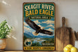 A vintage-style metal sign for the Skagit River Bald Eagle Natural Area, featuring an eagle in flight over a scenic landscape.