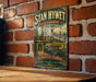A vintage-style sign for "Stan Hywet Hall & Gardens" in Akron, Ohio, featuring a brick wall and a garden scene.