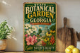 A vintage-style metal sign advertising the State Botanical Garden of Georgia, featuring a colorful illustration of flowers and a greenhouse.