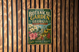 A vintage-style metal sign for the State Botanical Garden in Athens, Georgia, featuring a colorful illustration of flowers and a greenhouse.