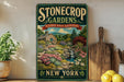A vintage-style sign for "Stonecrop Gardens" in New York, featuring a garden scene with a house, flowers, and a waterfall.