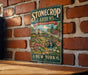 A vintage-style metal sign for "Stonecrop Gardens" is displayed on a brick wall, featuring a garden scene with a waterfall and flowers.