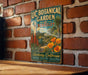 A vintage-style metal sign for the UC Botanical Garden in Berkeley, California, featuring a tropical garden scene with palm trees, flowers, and a tower.
