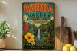 A vintage-style metal sign for Waimea Valley Botanical Garden in Hawaii, featuring colorful illustrations of tropical plants, flowers, and a waterfall.