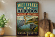 A vintage metal sign for the Wellfleet Bay Audubon Wildlife Sanctuary in Massachusetts, featuring an illustration of a heron and a lighthouse.