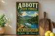 a vintage-style sign for Abbott State Forest in New Hampshire, with a scenic landscape depicting a lake surrounded by pine trees and mountains.