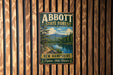 A vintage metal sign for Abbott State Forest in New Hampshire, featuring a scenic landscape with a lake and mountains.