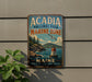 A vintage metal sign for Acadia National Park's Marine Zone, featuring a lighthouse and a seagull, is displayed on a wall next to a plant.