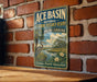 A vintage-style sign for the Ace Basin National Estuarine Research Reserve in South Carolina, featuring a seagull and a landscape with a river and palm trees.