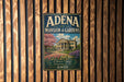 A vintage-style sign for "Adena Mansion & Gardens" is displayed on a wooden wall, featuring a large illustration of a mansion surrounded by a well-maintained garden.