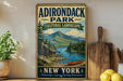 A vintage-style sign for Adirondack Park, New York, featuring a scenic landscape with a cabin, canoe, and mountains in the background.