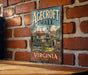 A vintage-style sign for Agedcroft Hall in Virginia, featuring a house illustration and the text "Agedcroft Hall" and "Agedcroft Hall in England in Virginia".