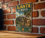 A vintage-style metal sign with the text "Ajanta Caves India" and an illustration of a temple or cave with a Buddha statue, hanging on a brick wall.