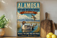 A vintage-style sign for the Alamo National Wildlife Refuge in Colorado, featuring a duck swimming in a lake surrounded by mountains.