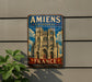 A vintage metal sign with the text "Amiens Cathedral" and "France" is displayed on a wall, featuring an illustration of the Notre-Dame Cathedral in Paris.