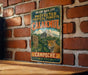 A vintage metal sign with text and an illustration of a jungle scene, mounted on a brick wall.