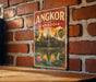 A vintage-style metal sign with the text "ANGKOR CAMDENIA" and an illustration of the Angkor Wat temple complex in Cambodia.