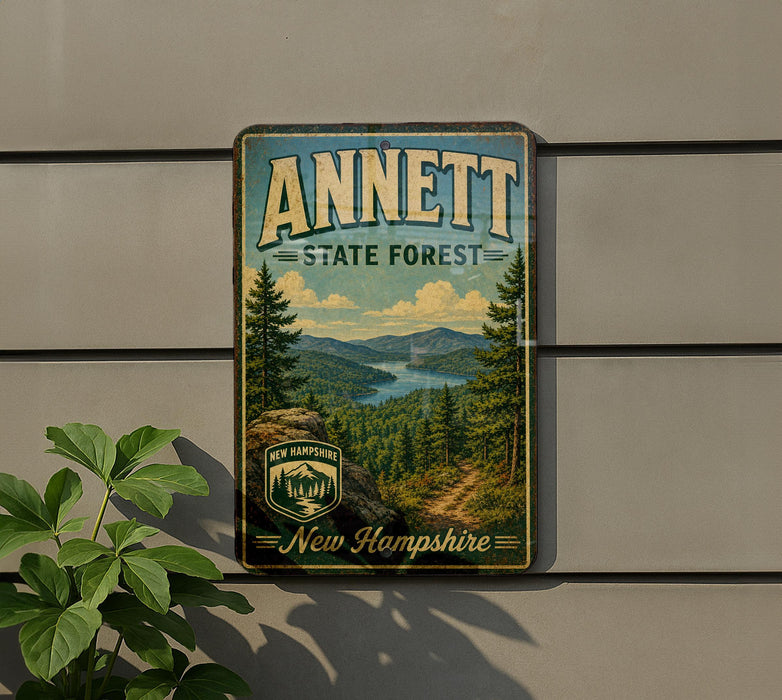 a vintage-style sign for the Annett State Forest in New Hampshire, with a scenic landscape of pine trees, mountains, and a river.