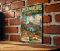 A vintage-style metal sign for Apache-Sitting Greaves National Forests in Arizona, featuring a scenic landscape with mountains, trees, and a lake.