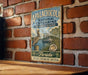 A vintage-style metal sign for the Apalachicola National Estuarine Research Reserve, featuring a pelican and a shell, is displayed on a brick wall.