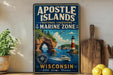 A vintage-style metal sign for the Apostle Islands National Lakeshore Marine Zone in Wisconsin, featuring a lighthouse, boats, and a scenic landscape.