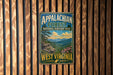 A vintage metal sign for the Appalachian Forest National Heritage Area in West Virginia, featuring a scenic landscape with mountains, trees, and flowers.