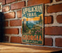 A vintage metal sign with the text "Appalachian Trail Georgia Walk the Legend" is displayed on a brick wall.