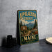 A vintage metal sign for the Appalachian Trail in Maine, featuring a scenic mountain landscape and a trail sign.