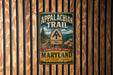 A vintage metal sign for the Appalachian Trail in Maryland, featuring a scenic illustration of the trail and the words "Appalachian Trail" and "A Footpath Through America".